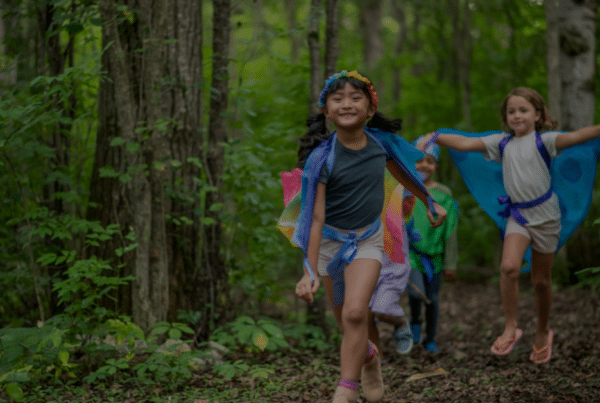 Three kids taking part in earth day activities by walking on a path in a forest with vibrant outfits